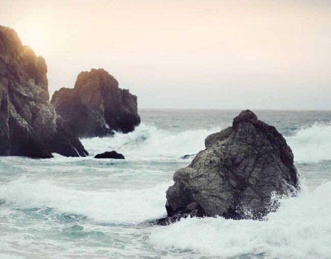Rocky coastline with waves crashing at sunset.