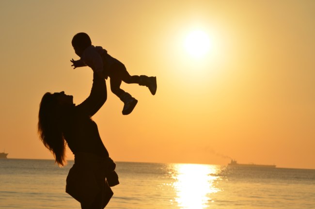 A silhouette of a parent lifting a child against a golden sunset over the water.