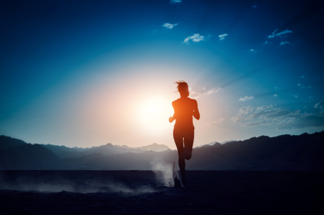Silhouette of a person running at sunrise with mountains in background.